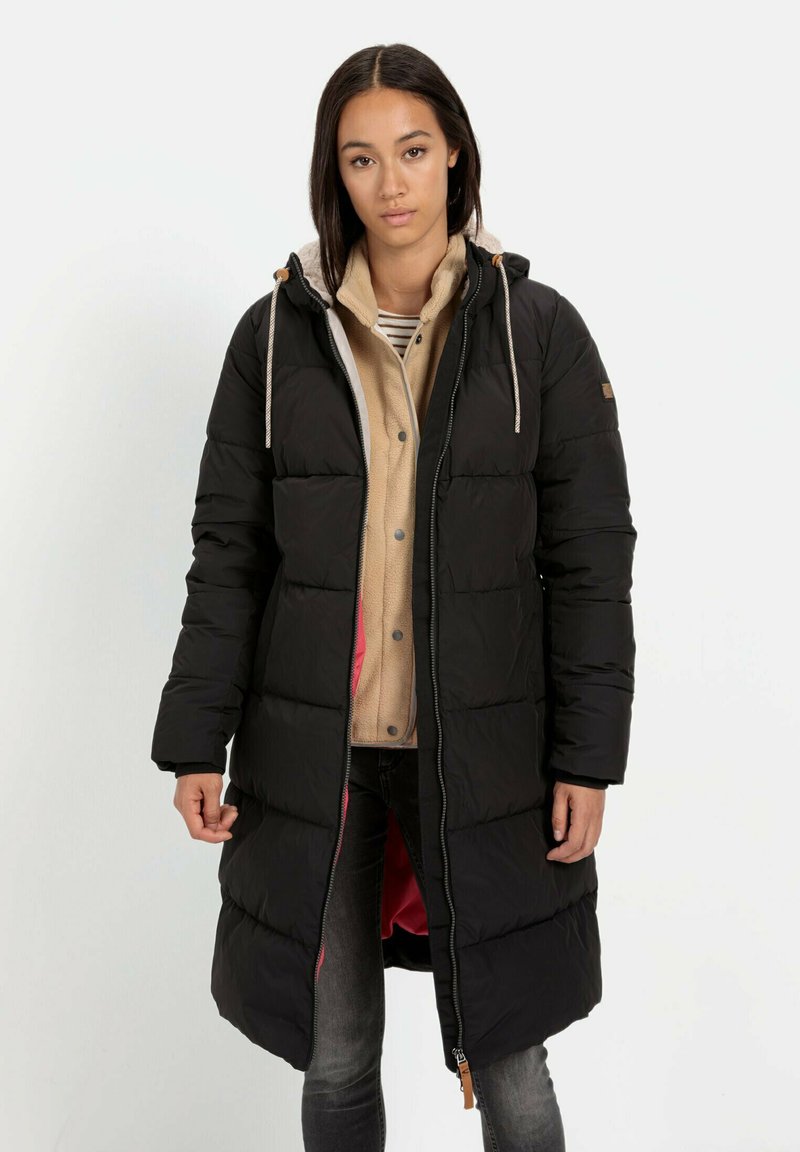 Lange zwarte pufferjas met capuchon, rits aan de voorkant en trekkoorden. Gevoerd met roze stof, gelaagd over een beige fleece sweater en gestreept shirt.