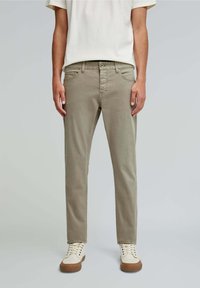 Pantaloni din bumbac de culoare khaki deschis, cu o croială ajustată, cinci buzunare și o textură netedă. Asortați cu adidași crem cu tălpi de cauciuc maro.