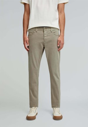Pantalons en coton khaki clair avec une coupe slim, cinq poches et une texture lisse. Associés à des baskets crème avec des semelles en caoutchouc brun.