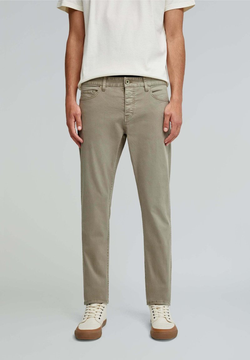 Pantaloni din bumbac de culoare khaki deschis, cu o croială ajustată, cinci buzunare și o textură netedă. Asortați cu adidași crem cu tălpi de cauciuc maro.