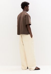 Braunes kurzärmliges Hemd mit lockerer Passform, kombiniert mit beigen weit geschnittenen Hosen. Das Outfit zeichnet sich durch ein minimalistisches Design und eine entspannte Silhouette aus.