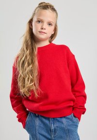 Red knitted sweater with long sleeves and a ribbed round neckline, worn with high-waisted denim jeans, featuring a relaxed fit.