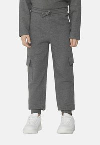 Szare spodnie cargo wykonane z miękkiego materiału, z bocznymi kieszeniami, elastycznym pasem ze sznurkiem oraz dopasowanymi mankietami. Noszone z białymi trampkami.