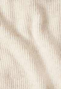 Tessuto di colore crema chiaro con una texture a coste, caratterizzato da fibre morbide e fini che creano onde e pieghe delicate in tutto il tessuto.
