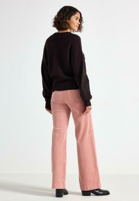 Brun oversized sweater med ribbet kant, parret med lyserøde fløjlsbukser med flared ben og sorte ankelstøvler, set bagfra.