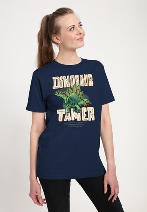 Tyrkysové tričko s krátkým rukávem, na kterém je grafika dinosaura a text "Dinosaur Tamer" v tučném, krémovém a oranžovém písmu.
