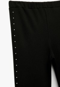 Sorte leggings med en struktureret stof, der har en bred elastisk talje og en lodret række af små sølvnitter langs den ene side.