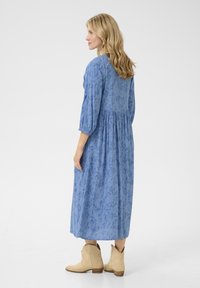 Abito lungo in tessuto azzurro chiaro con un motivo floreale, maniche a tre quarti, vita impero, abbinato a stivali cowboy beige.