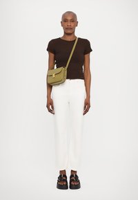 Top tricotat texturat în nuanțe de maro, blugi albi cu croială dreaptă, sandale platformă negre și geantă crossbody verde cu un accent de aur.