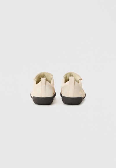 Chaussures en suède beige clair avec un bout arrondi, semelle en caoutchouc noir et languette à l'arrière ; texture subtile et design minimaliste.