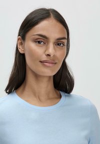 Vaaleansininen pyöreän kaula-aukon T-paita, joka on valmistettu pehmeästä kankaasta. Ominaisuuksiin kuuluvat lyhyet hihat ja sileä pinta, joka istuu tiiviisti vartaloon.