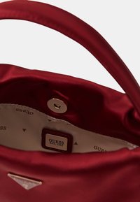 Czerwony satynowy torebka wewnętrzna z etykietą logo i zapięciem na magnes. Podszewka ma powtarzający się wzór trójkątów.