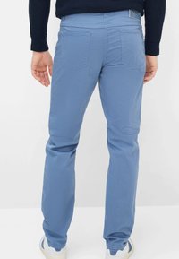 Hellblaue Baumwollhose mit geraden Beinen, zwei Gesäßtaschen, kontrastierender Naht und einem Etikett am Bund. Glatte Textur.