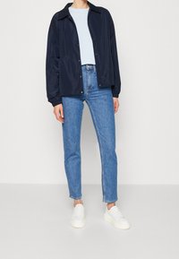 Lekka granatowa kurtka z kołnierzem, zapięciem na zatrzaski i elastycznymi mankietami, zestawiona z jasnymi dżinsami i białymi trampkami.