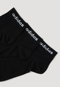 Calzini neri in cotone con punta e tallone rinforzati, bordo elastico con logo "adidas" bianco. Tessuto morbido, senza schemi o accenti visibili.
