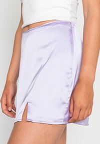 Saia de cetim lavanda com fenda lateral, textura suave e fecho de zíper discreto no lado esquerdo, perto da linha da cintura.