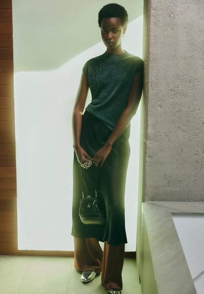 Sparkling green short-sleeve top paired with a black skirt, brown trousers, and silver shoes; holding a small black textured handbag.