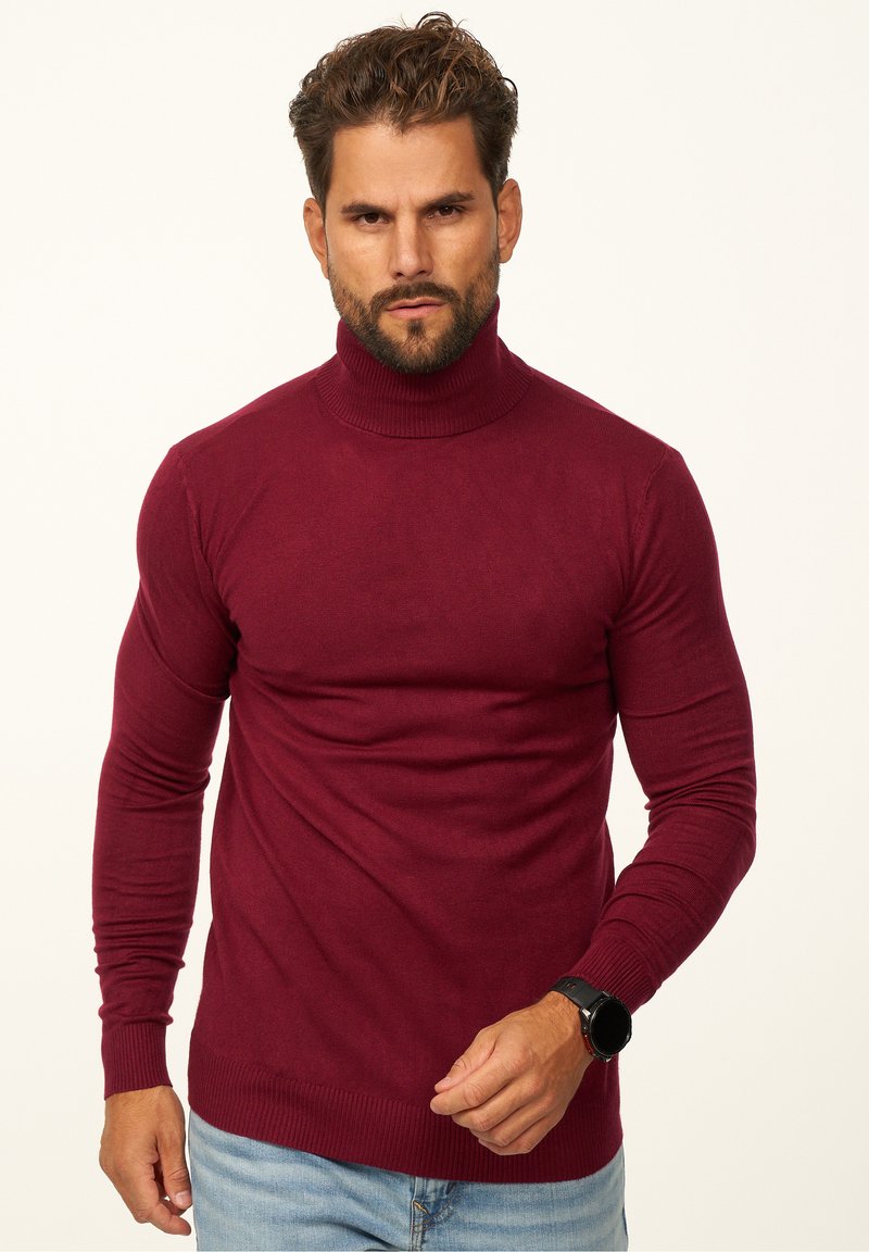 Bordeauxfarbener Rollkragenpullover mit körperbetontem Design, langen Ärmeln und gerippten Bündchen sowie Saum. Hergestellt aus einem weichen Material, getragen mit hellblauen Jeans.