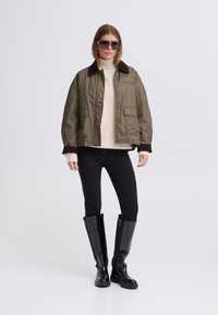 Olívazöld, rövid fazonú dzseki barna kordbársony gallérral, krémszínű kötött pulóver, fekete skinny farmer és fekete térdig érő csizma.