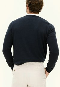 Marinblå stickad tröja med rundad hals och långa ärmar, tillverkad av ett mjukt material, i kombination med ljusa byxor.