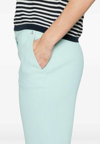Pantaloni slim fit di un blu chiaro con una finitura texturizzata, dotati di una tasca e un piccolo logo "A" argentato vicino alla vita, abbinati a una maglietta a righe blu navy.