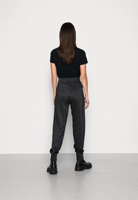 Černé tričko, pohled zezadu, spárováno s volnými černými tepláky s jemnou třpytivou texturou a elastickými manžetami. Černé kotníkové boty dotvářejí celý vzhled.