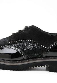 Chaussure oxford noire en cuir verni et en daim, ornée de clous métalliques le long des coutures et d'une semelle noire texturée.