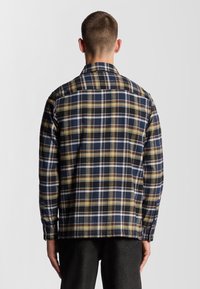 Camicia a quadri nei colori navy, nero, giallo e bianco; con bottoni, colletto e maniche lunghe; tessuto morbido e intrecciato con una vestibilità comoda.