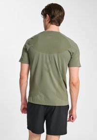 Oliwkowo-zielona sportowa koszulka z krótkim rękawem, lekka tkanina, dopasowany krój, z subtelnymi tłoczonymi wzorami na plecach, zestawiona z czarnymi szortami.