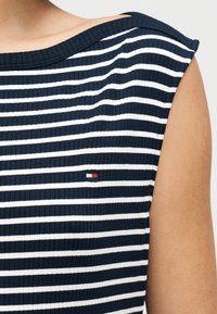 Μπλούζα με ριγέ σχέδιο σε ναυτικό μπλε και άσπρο με ραβδωτή υφή, φαρδύ ντεκολτέ και κοντά μανίκια. Διαθέτει μικρό σήμα λογοτύπου σε κόκκινο, άσπρο και μπλε.