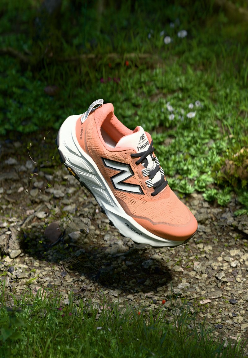 Chaussure de course légère avec une tige en maille corail respirante, des accents noirs, une semelle intercalaire blanche épaisse et une semelle extérieure avec une texture de grip, flottant au-dessus du sol.