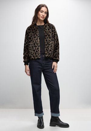 Chaqueta bomber de piel sintética con estampado de leopardo y puños de canalé negros, combinada con jeans rectos de color azul oscuro y botas de tobillo negras.
