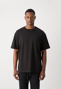 Sort bomulds t-shirt med rund hals, korte ærmer og en brystlomme. Designet er simpelt og afslappet. Minimalistisk æstetik.