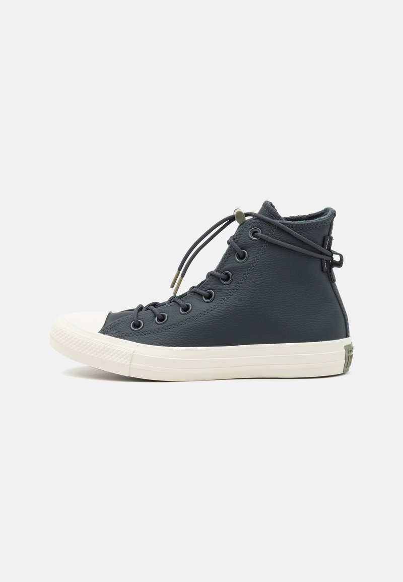 Zapatillas altas de cuero gris oscuro con suela de goma crema y puntera. Cuentan con seis ojales y cordones en bucle para un ajuste seguro.