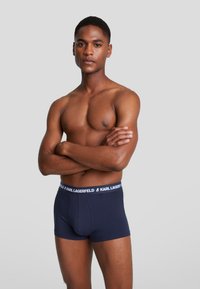 Sötétkék boxer alsónemű, puha anyagból, kontrasztos fehér "KARL LAGERFELD" logós derékpánttal és testhezálló fazonnal.