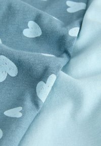 Vaaleansininen kangas, jossa on pieniä valkoisia sydämen kuvioita, pehmeällä pinnalla ja hienovaraisilla sävyvaihteluilla, kauniisti laskostettuna syvyyden ja yksityiskohtien näyttämiseksi.