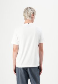 White short-sleeve t-shirt made of cotton, featuring a simple round neck, straight cut, and a small black tag at the back.