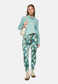 Light blue long-sleeve top, patterned leggings with turquoise, brown, and cream diamonds, beige ankle boots, and a white handbag.