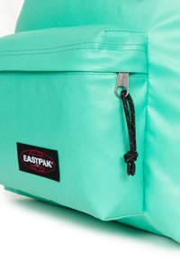 Zaino di un verde teal chiaro con superficie testurizzata, dotato di una tasca frontale, chiusura con cerniera e etichetta di branding nera.