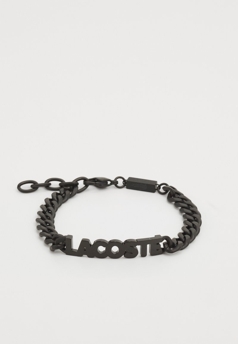Crna metalna lancana narukvica s odvažnim, uzdignutim logotipom "LACOSTE" i sigurnom kopčom. Dizajn ima glatku, sjajnu teksturu.