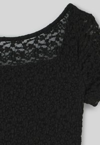 Haut en dentelle noire avec un col large décolleté et des manches courtes. La texture présente un motif floral avec une finition douce et transparente.