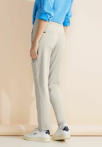 Ljust grå byxor med skräddarsydd passform, har sidofickor och en slät textur, kombinerat med vita sneakers och en blå topp.