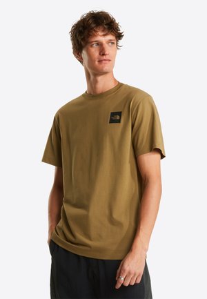 T-shirt in cotone verde oliva con scollo rotondo, maniche corte e una piccola toppa con logo nero sul lato sinistro del petto. Design semplice.