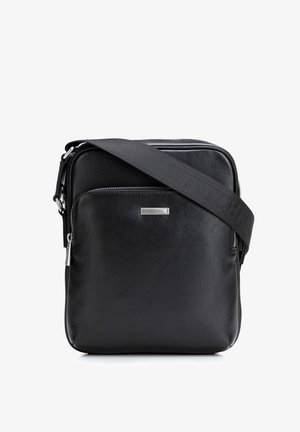 Zwarte leren crossbodytas met voorritszak, zilveren logoplaatje en verstelbare zwarte stoffen band met reliëfmerk van de merknaam.