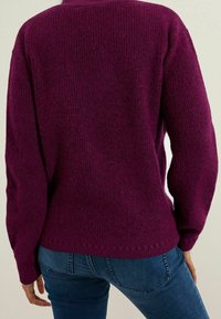 Suéter de punto morado con acabado texturizado, mangas largas y un ajuste holgado, combinado con vaqueros azules. Costuras visibles en el dobladillo.