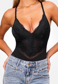 Body de encaje negro con escote pronunciado, tirantes ajustables y un panel de malla transparente en la cintura. Combinado con pantalones cortos de mezclilla azul claro.