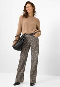Maglione beige lavorato a maglia, pantaloni a gamba larga con motivo in marrone e grigio, cintura nera e borsa nera. Modella con capelli mossi in piedi su uno sfondo chiaro.