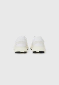 Baskets de sport blanches avec une tige en mesh, un col rembourré et une semelle texturée avec des accents noirs. Design simple avec une construction légère.