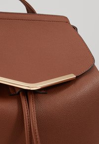 Borsa in pelle marrone con texture e patta geometrica. Accenti in metallo dorato alla chiusura, con un design pulito e cuciture distintive.