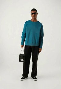 Teal sweatshirt med ribbad mudd, parat med svarta vida byxor. Tillbehören inkluderar svarta solglasögon och en liten svart väska med logotyp.